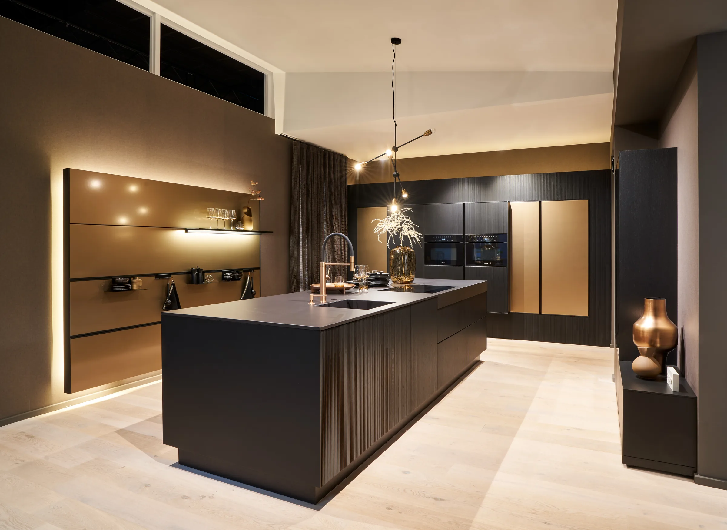Dunkle Kücheninsel mit Bronzefronten und Pendelleuchte im Showroom von Gerdum Küchen in Saarlouis